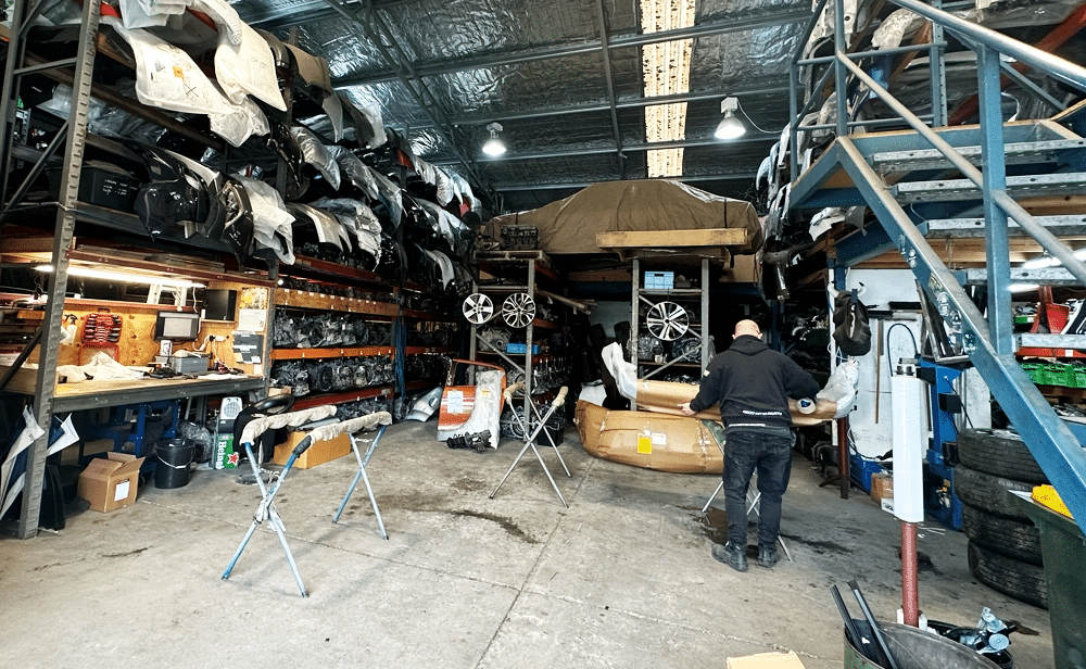 A long warehouse aisle with shelves stacked high with a large inventory of used car doors in various colors